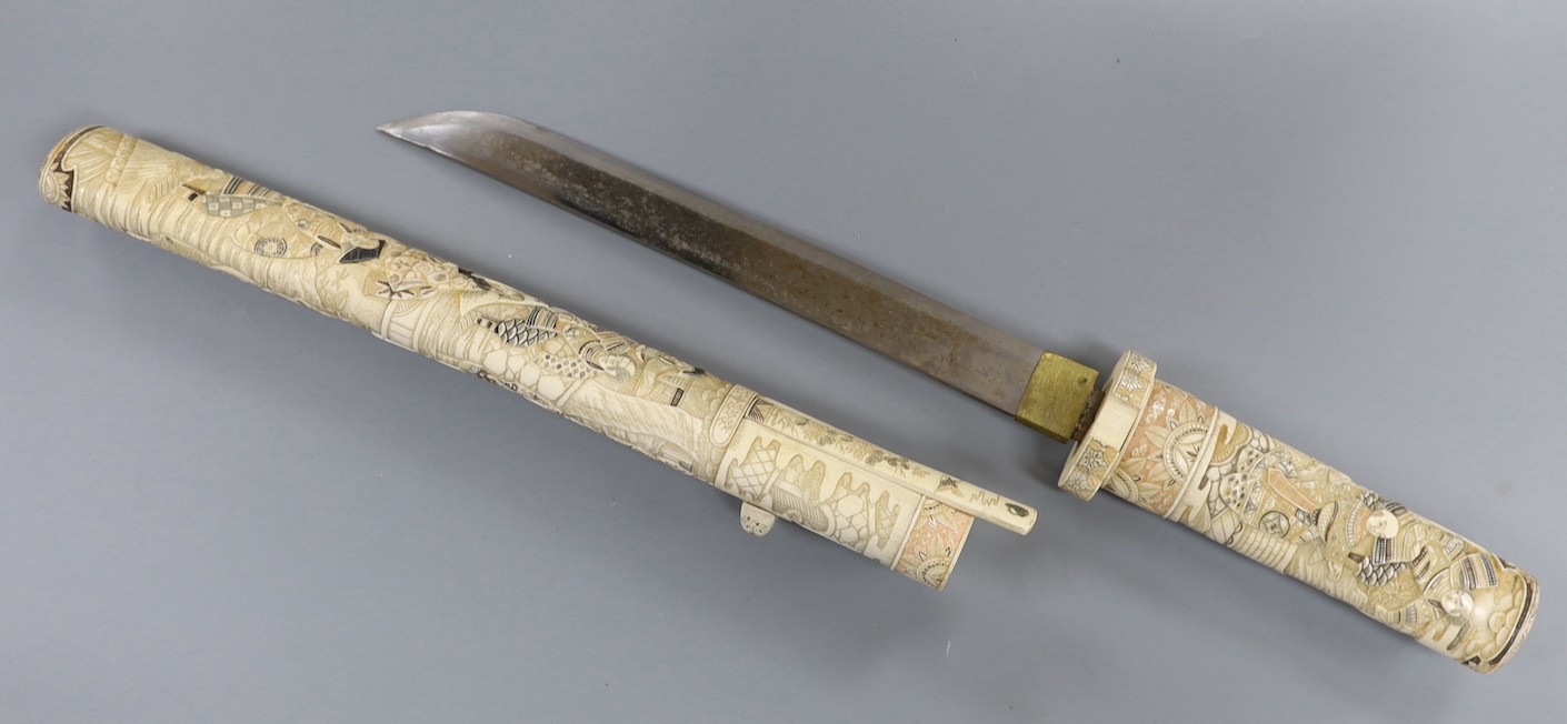 A Japanese carved and coloured ivory tanto, Meiji period, the hilt and scabbard carved to both sides with figures in ceremonial dress, the whole etched in black , green and red, the separate kodzuka with ivory blade and